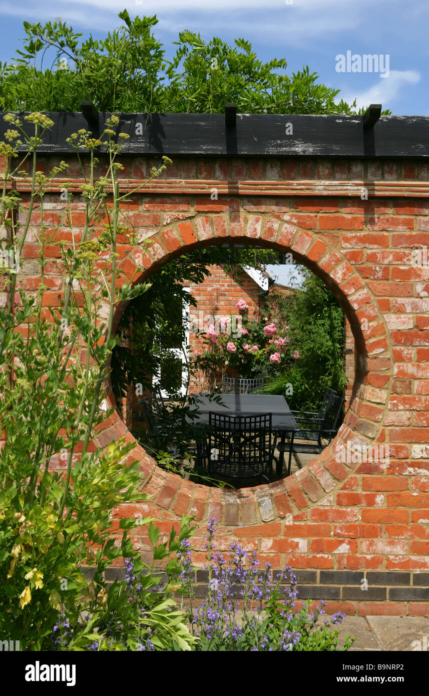 View into a walled garden through circular hole in terracotta brick wall. Stock Photo