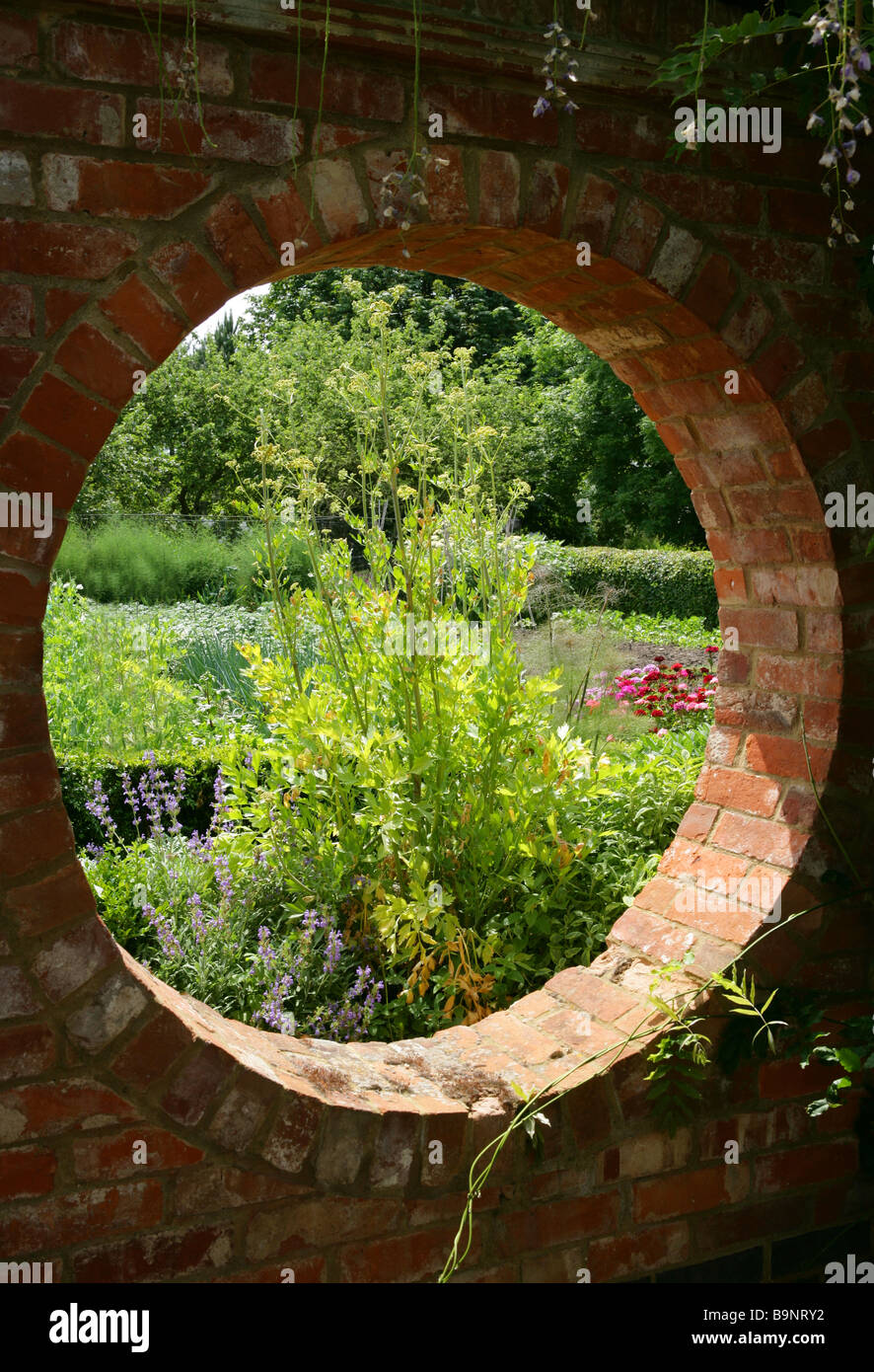 View through a circle hole in a bricked garden wall into a summer garden. Stock Photo