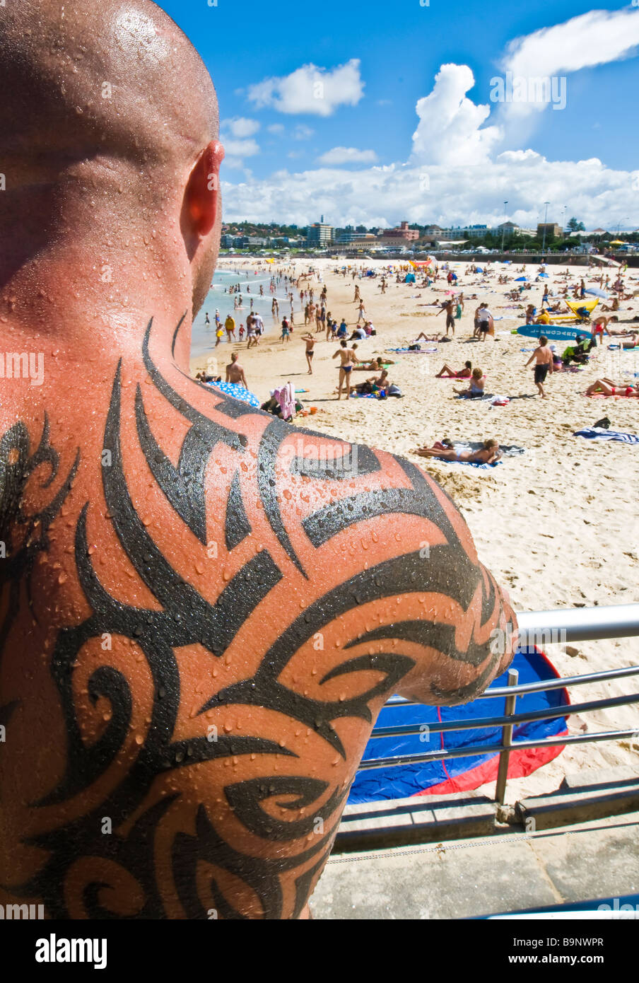 Tattooed beefcake guards his turf on a Summer day at Bondi Beach Australia as a packed beach soaks up the sun. Stock Photo
