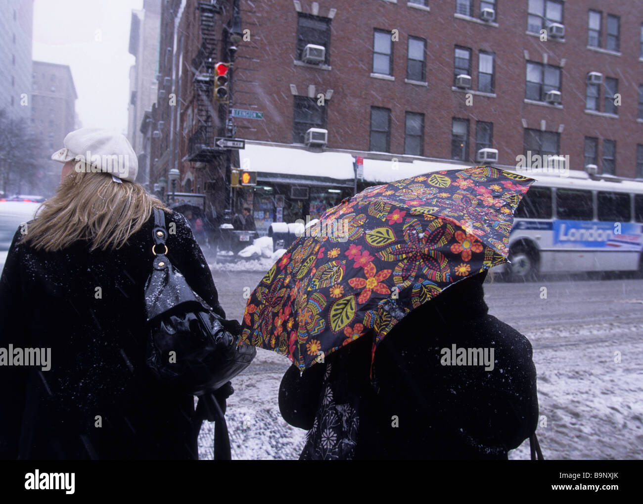 New York City winter weather. People crossing street at bus stop. Street-corner open umbrella. Snow Stock Photo