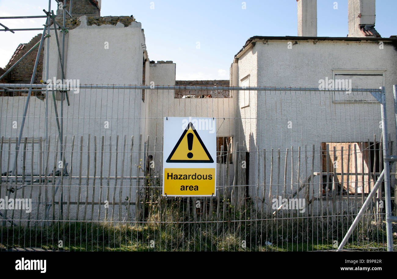 Warning sign attached to fencing outside a burnt out derelict building. It reads 'Hazardous area' Stock Photo