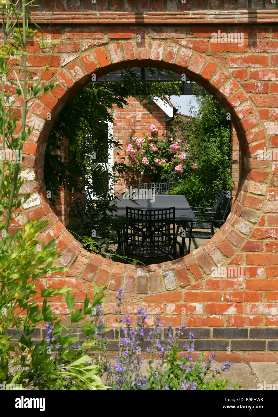 View into a walled garden through circular hole in terrcotta brick wall,england. Stock Photo