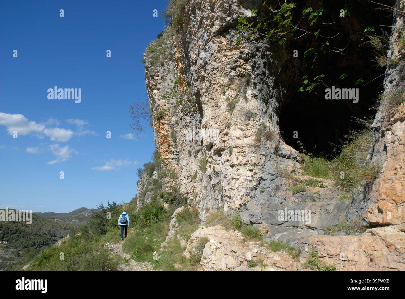 woman walking on path by cave entrance off a Mozarabic trail, Vall de Laguart, Benimaurell, Alicante Province, Comunidad Valenci Stock Photo