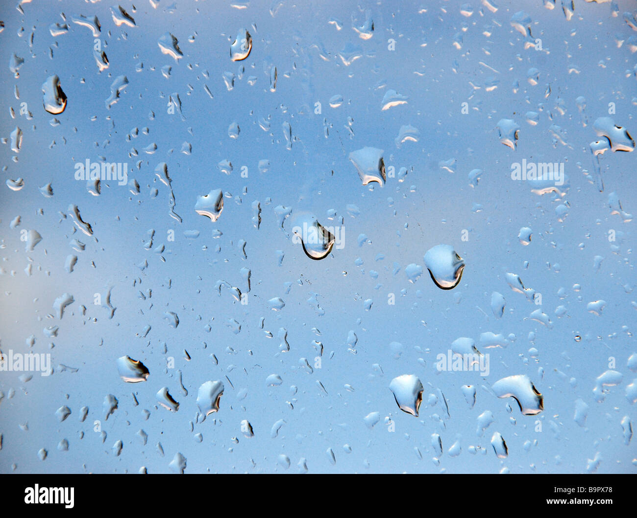 Rain drops on a window pane, looking out to a brightening sky. Stock Photo
