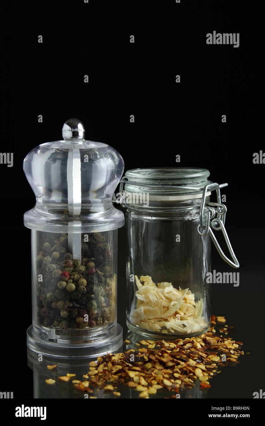 Pepper mill and glass jar with scattered spice against black background