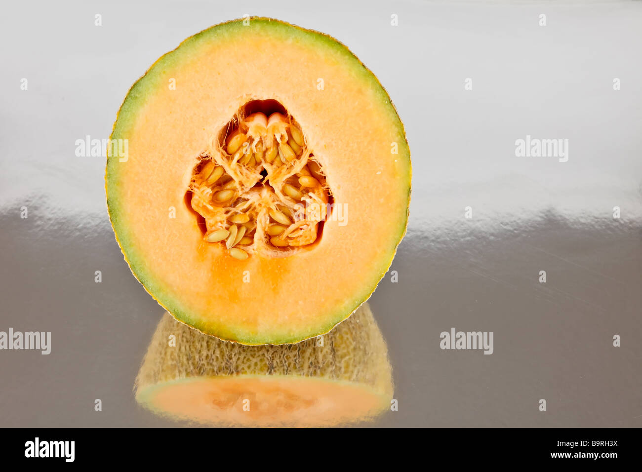 rock melon cantaloupe halved on a reflective surface with seeds Stock Photo