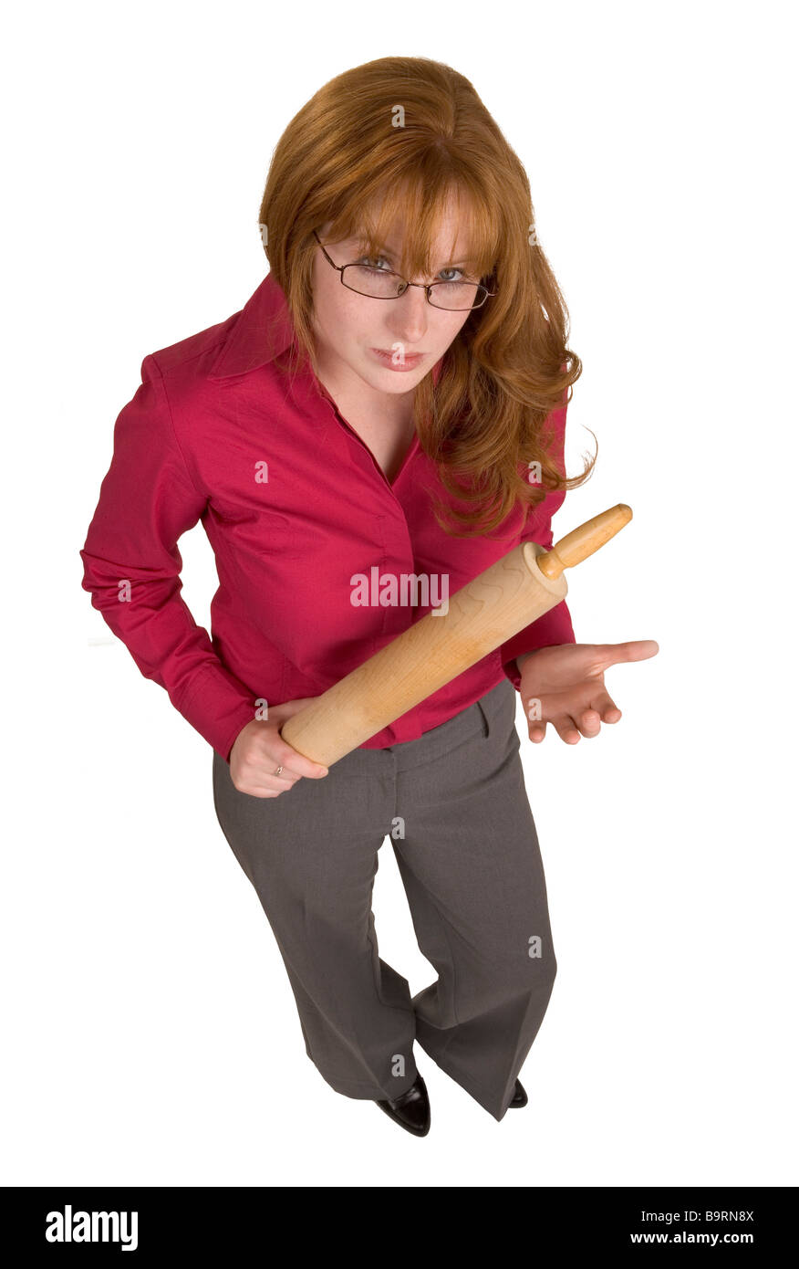 An angry redheaded woman with a wooden rolling pin holing it in a menacing way Stock Photo