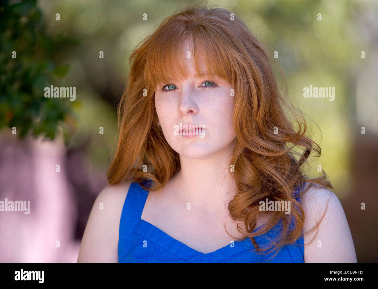 An outdoor portrait of a young red headed woman in a blue dress Stock Photo