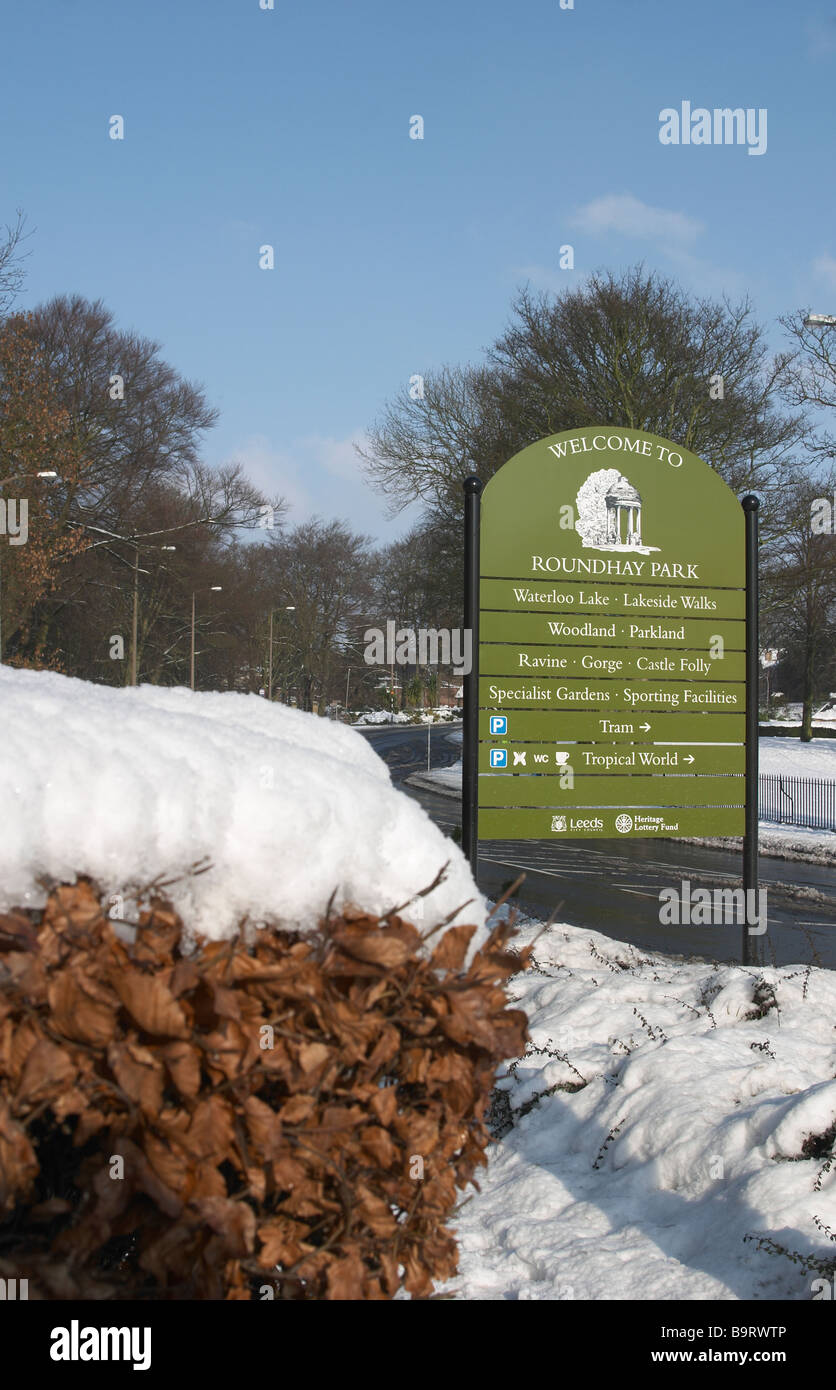Snow scene with trees and shrubs and hedge Road running through with Welcome to Roundhay Park sign Stock Photo