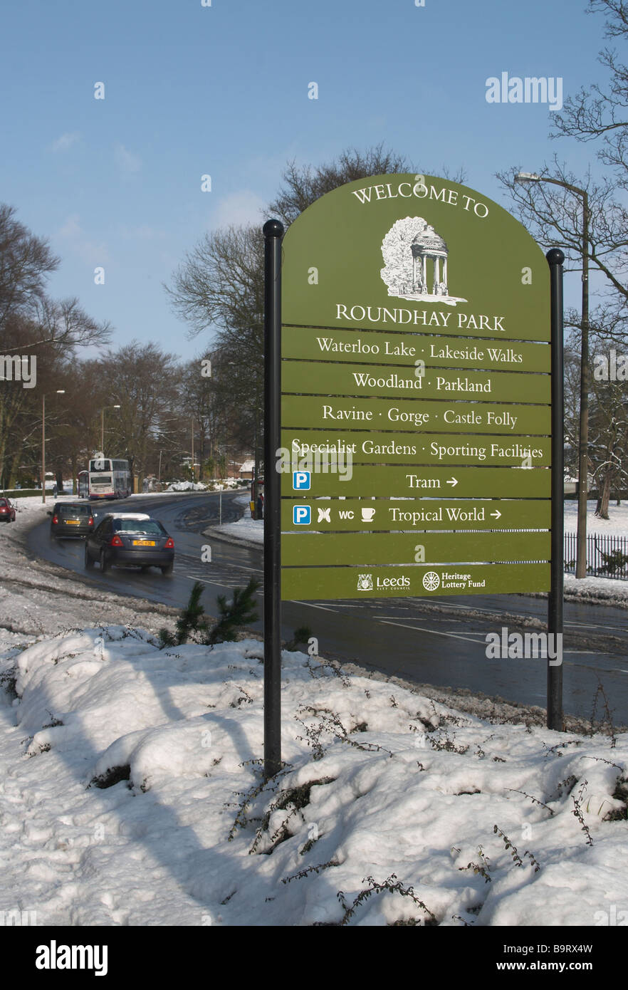 Snow scene with trees and shrubs and hedge Road running through with Welcome to Roundhay Park sign Stock Photo