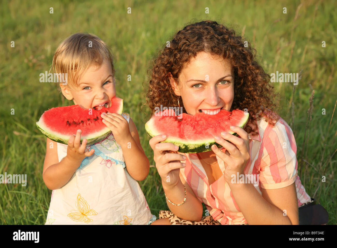 mother and daughter eat watermelon on the grass Stock Photo