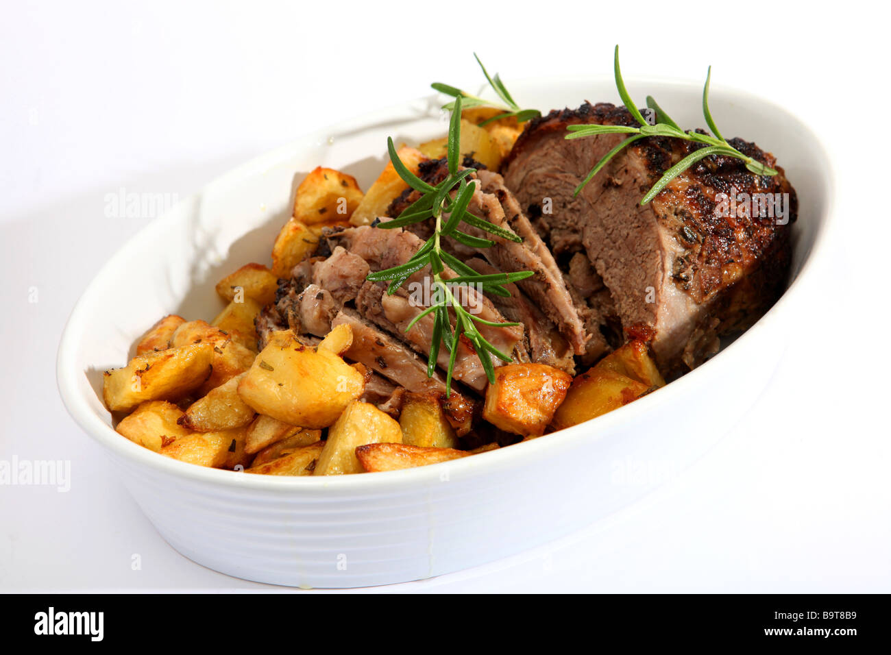 A carved joint of lamb in a serving dish with herbed diced roast