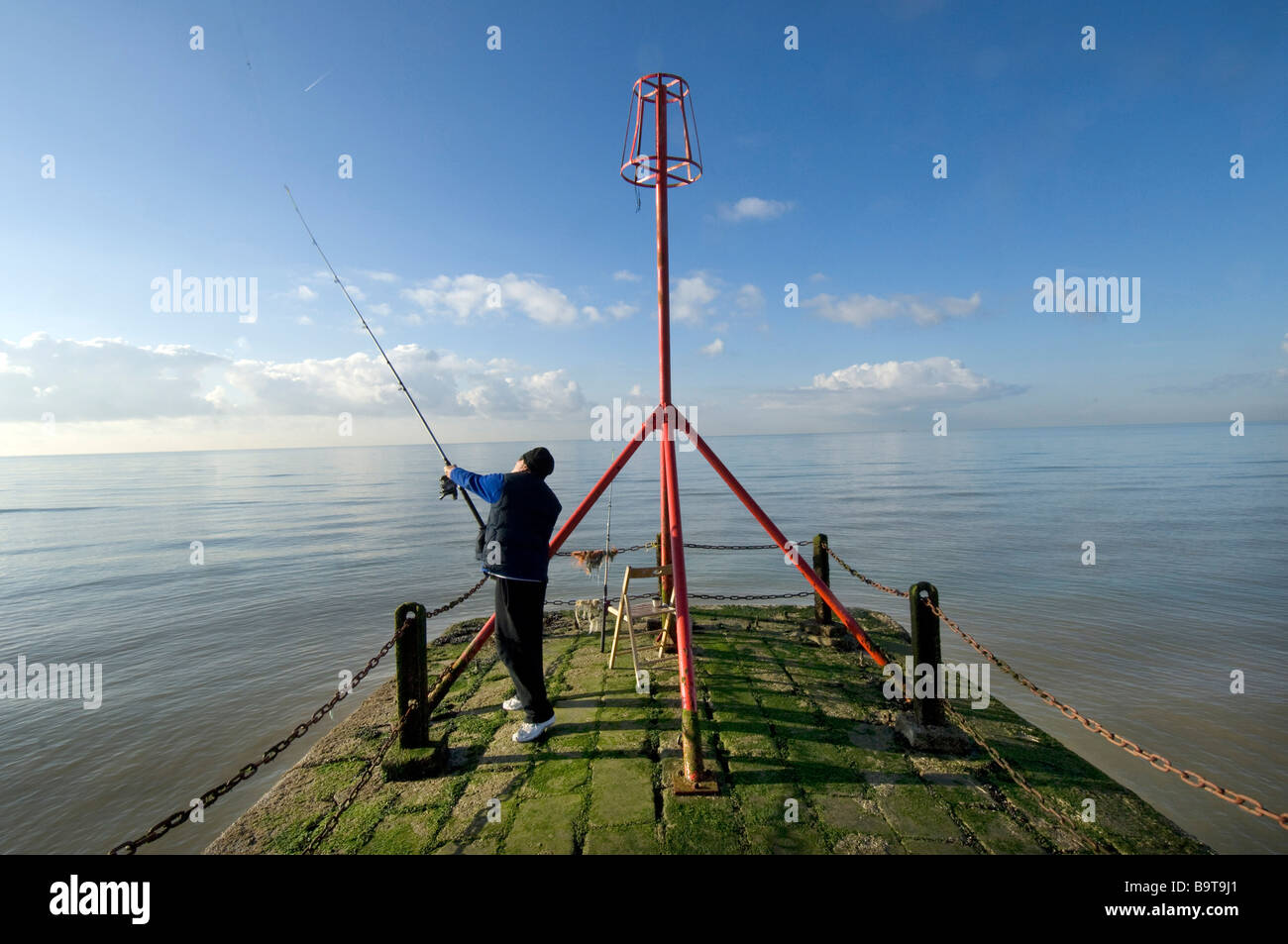 A man casting a fishing line from the end of a jetty on Brighton