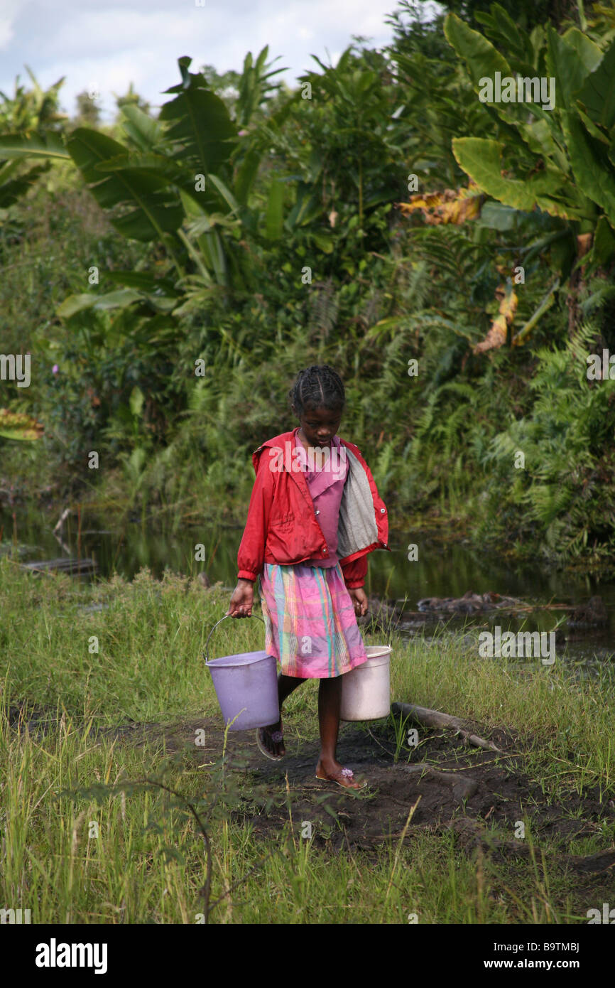 A young girl collects water from a dirty stream, Madagascar, Africa Stock Photo