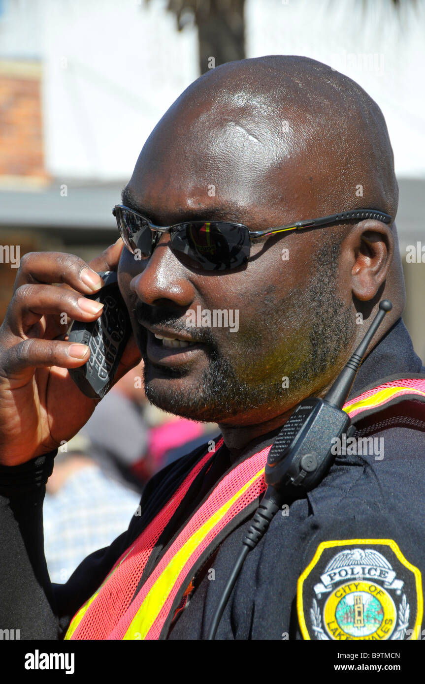 African American Police Officer Uses Phone While Managing Crowd Stock Photo