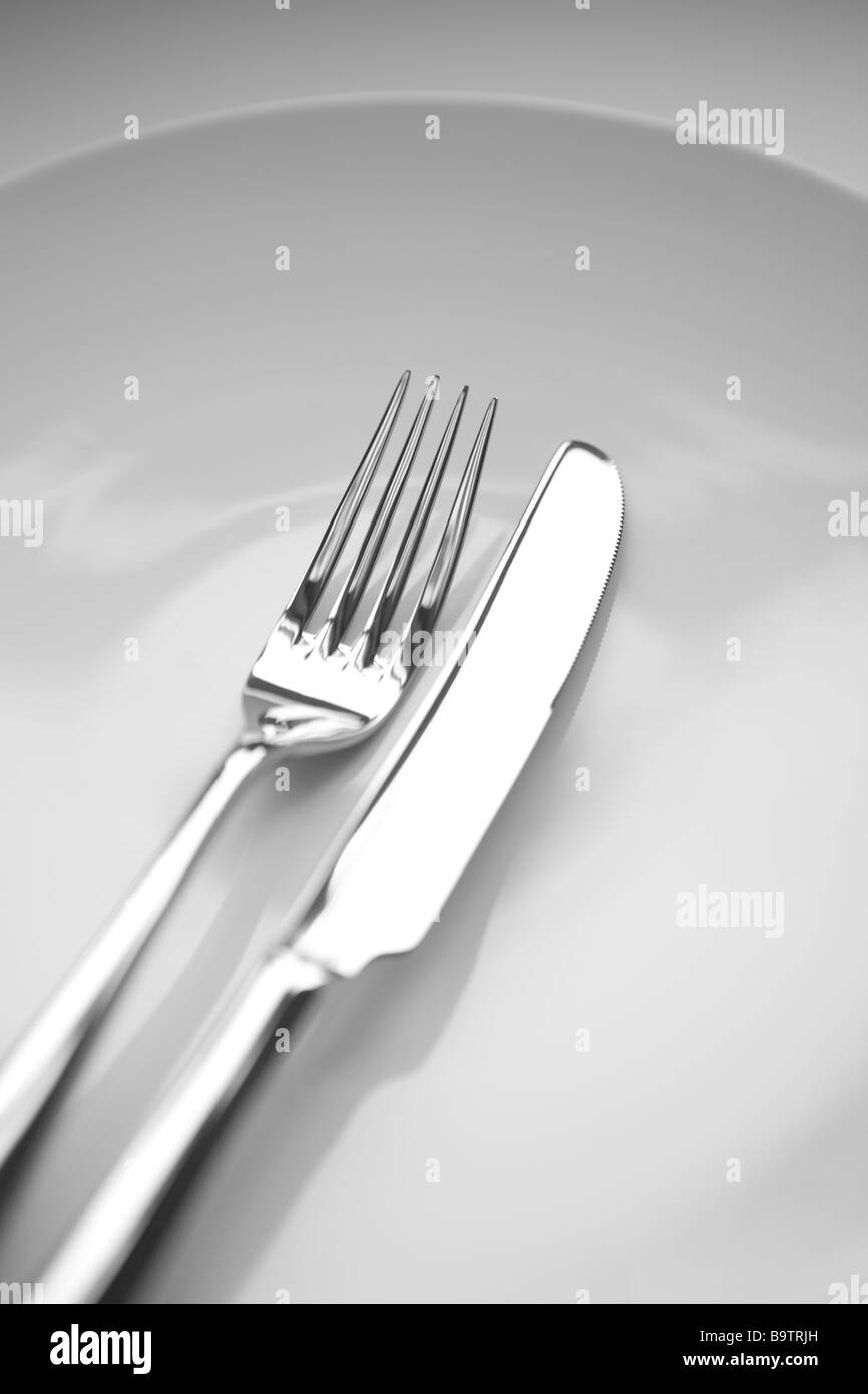 stainless steel knife and fork on a white plate and background. Very thin depth of field Stock Photo