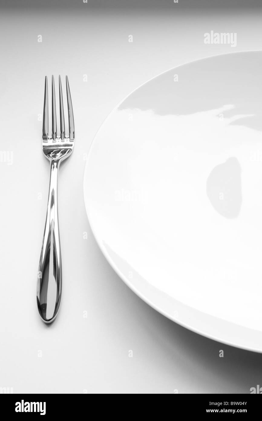 Stainless steel fork sits alongside a clean white plate on a white background Stock Photo