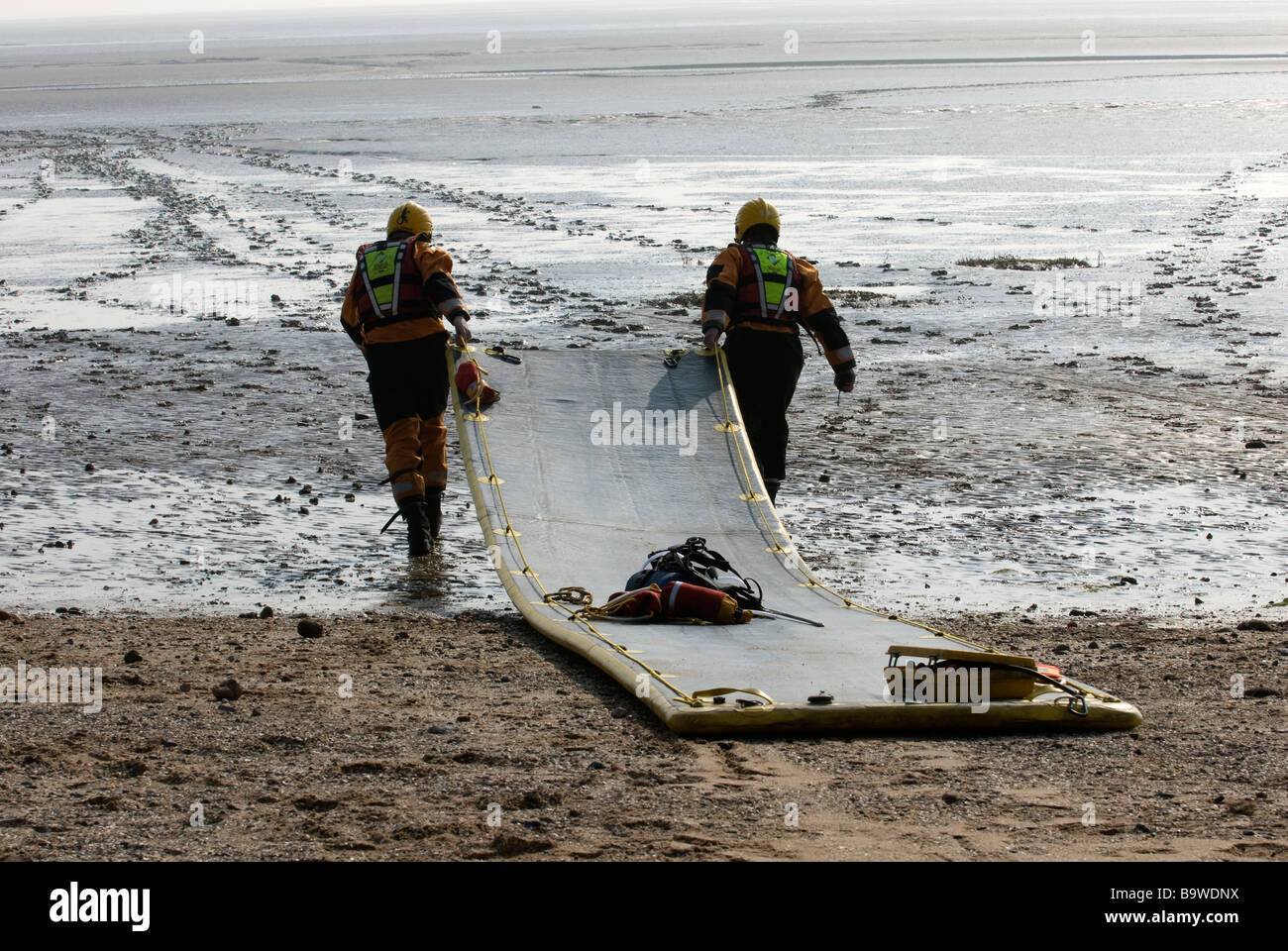 Two firefighters drag inflatable mud rescue mat out onto mud bank to