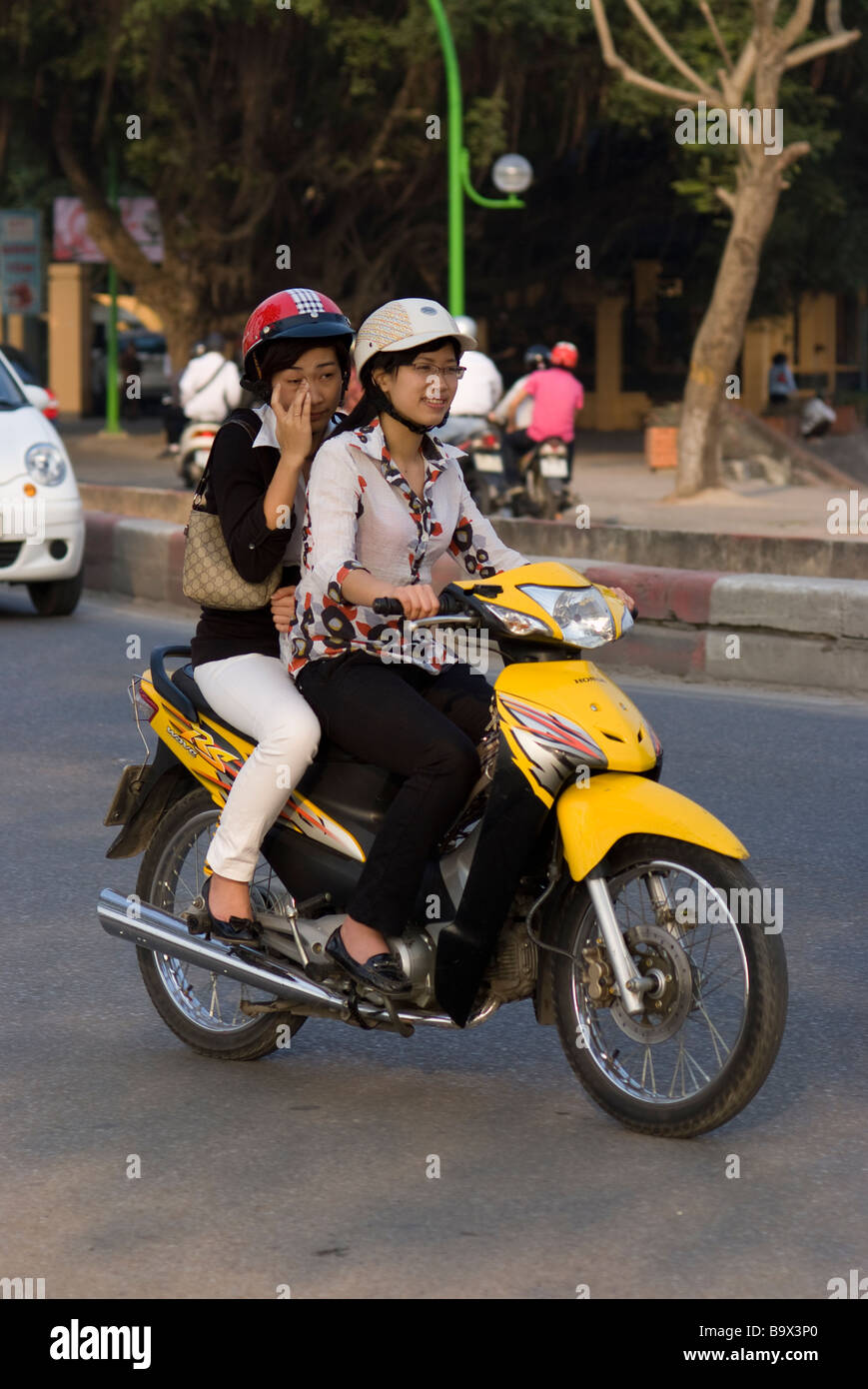 Two women riding a yellow Honda motorbike in Hanoi Vietnam Stock Photo