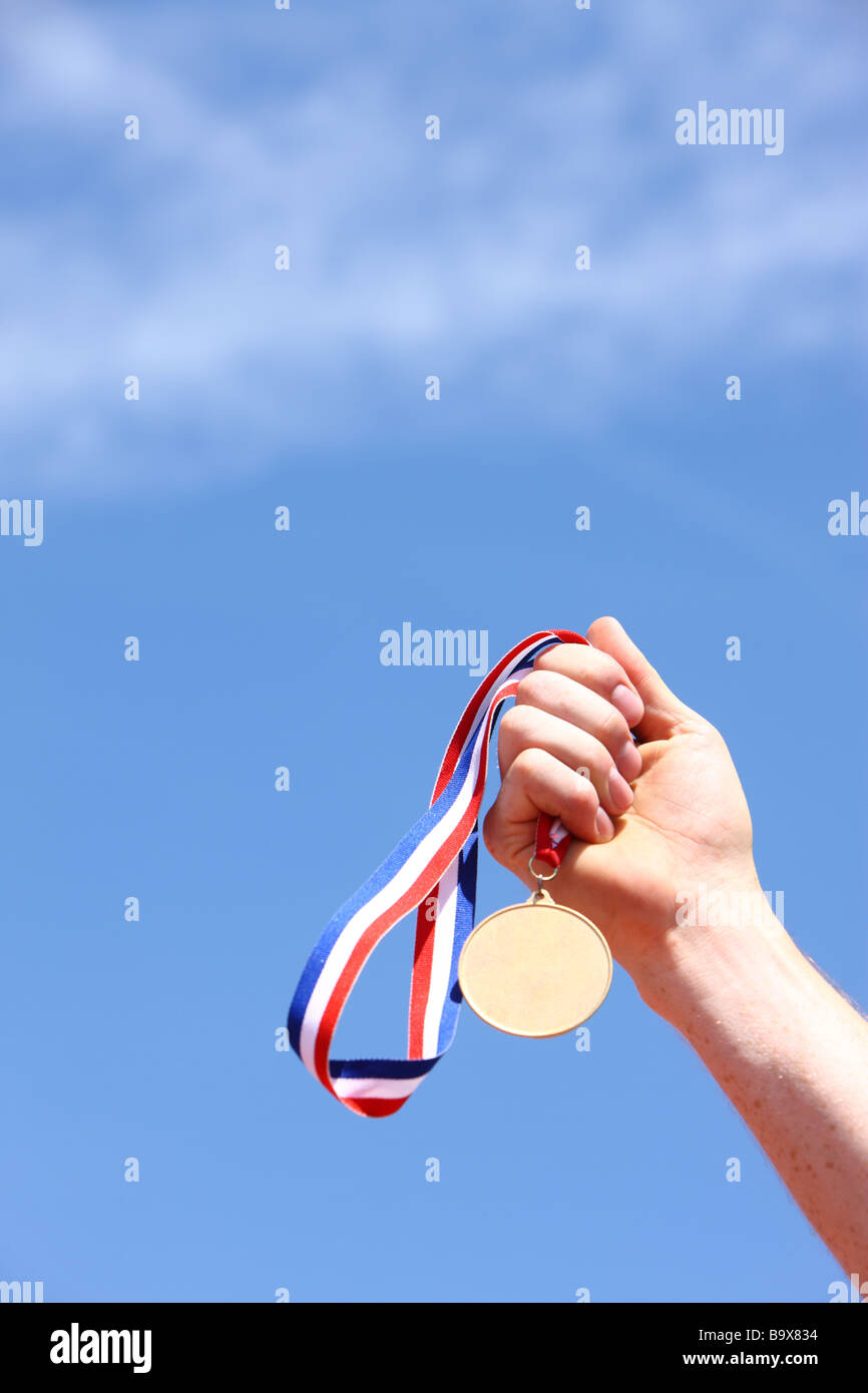 Hand holding gold medal against blue sky Stock Photo - Alamy