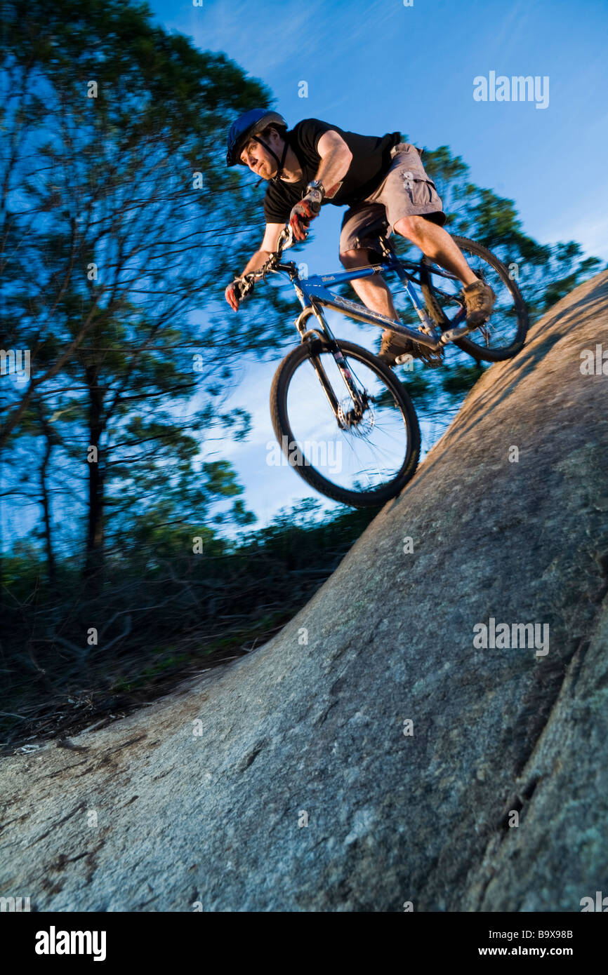 A mountain biker rides down a large steep rock with sky in background ...
