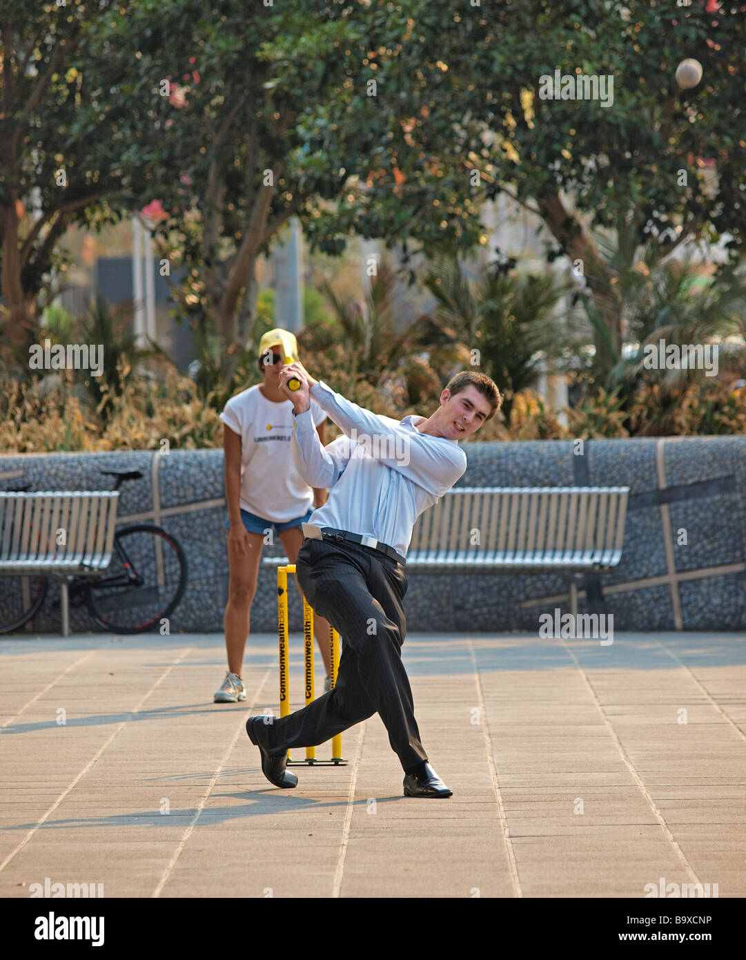 OFFICE WORKER PLAYING STREET CRICKET, POWERFUL STRIKE OF BALL,  SOUTHBANK MELBOURNE VICTORIA AUSTRALIA Stock Photo