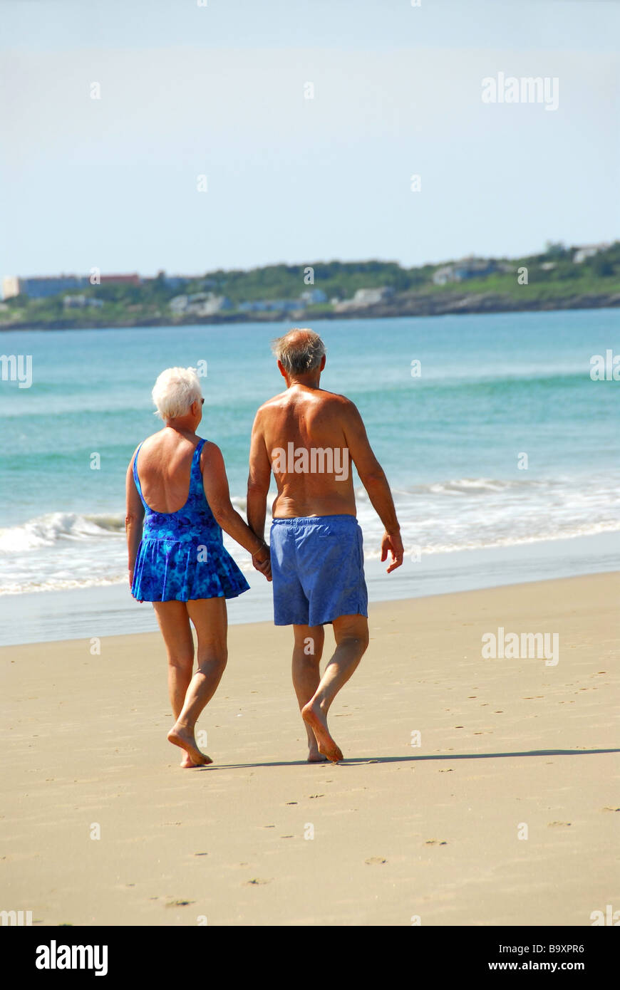 Happy retired couple taking a walk on a beach holding hands Stock Photo