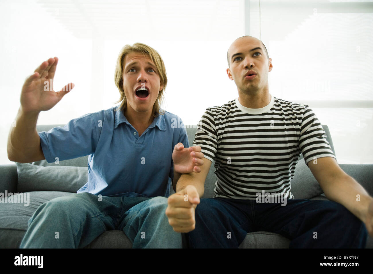 Two men sitting on sofa watching TV, hands in air Stock Photo