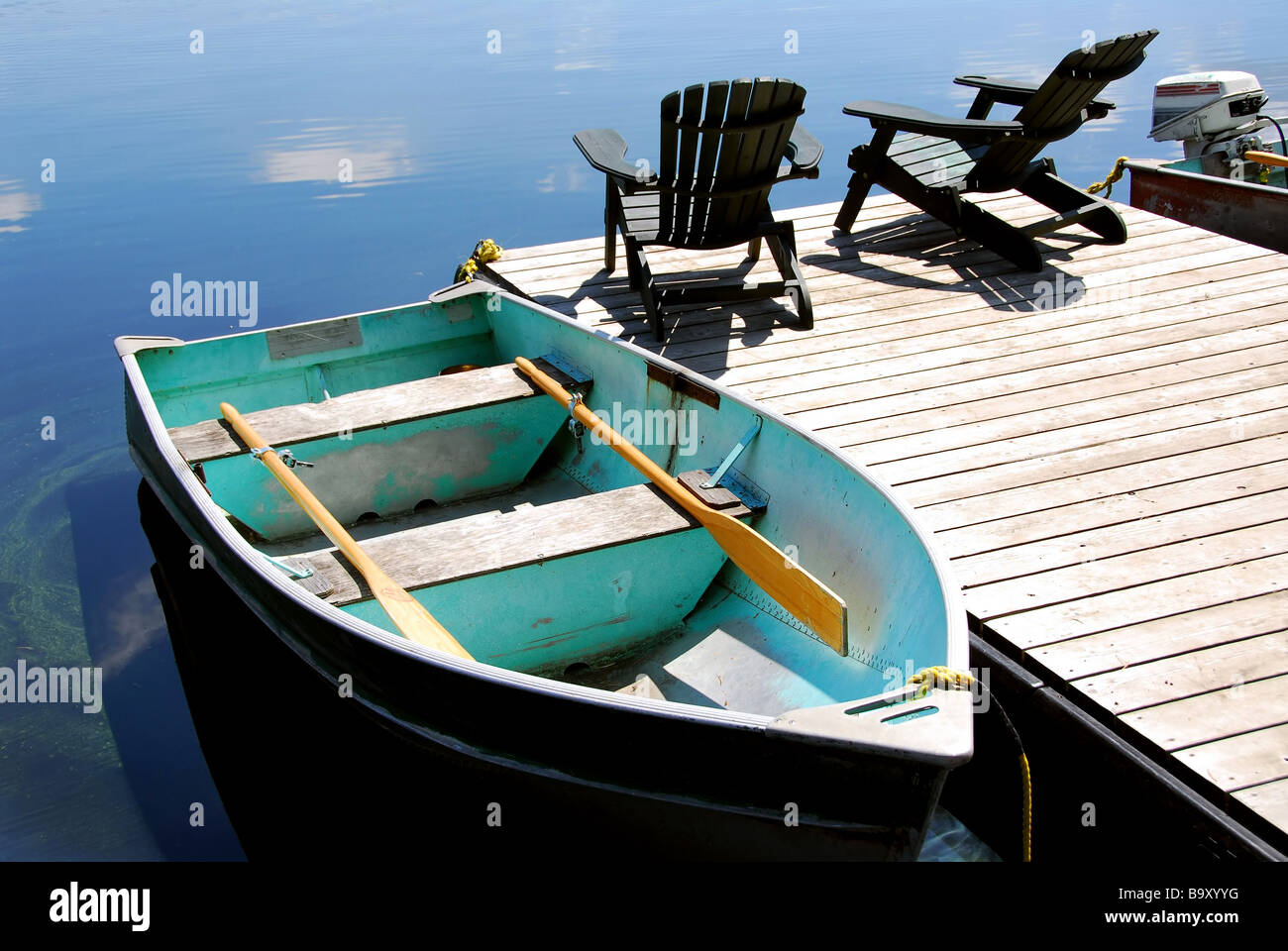 Two wooden adirondack chairs on a boat dock on a beautiful still lake