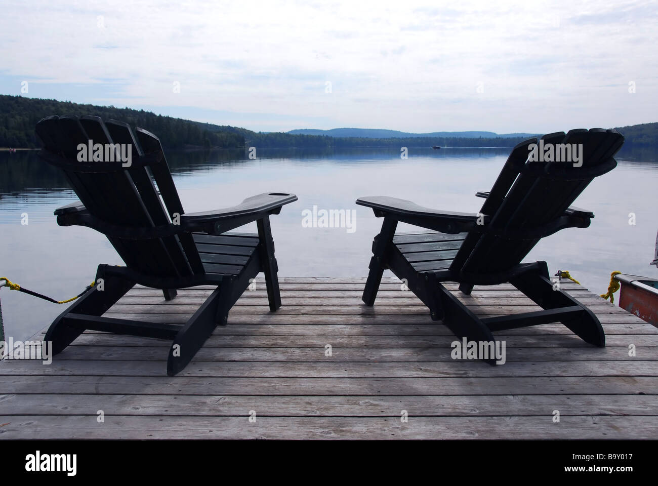 Two wooden adirondack chairs on a boat dock on a beautiful lake in the