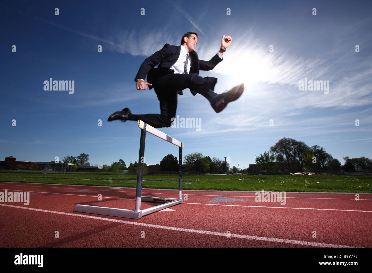 Businessman jumping over track hurdle Stock Photo Alamy