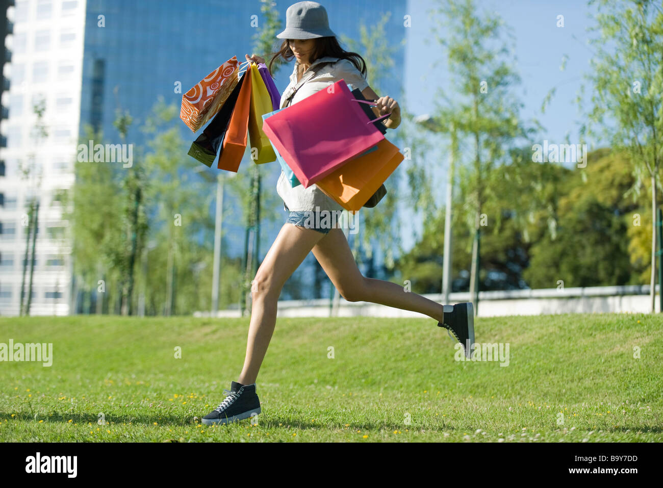 Young woman running through park, carrying several shopping bags Stock