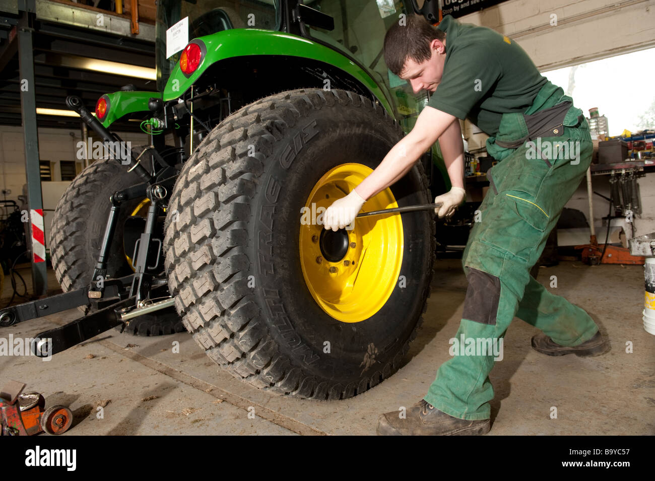 Garage worker manually tightening the wheel bolts on a John Deere