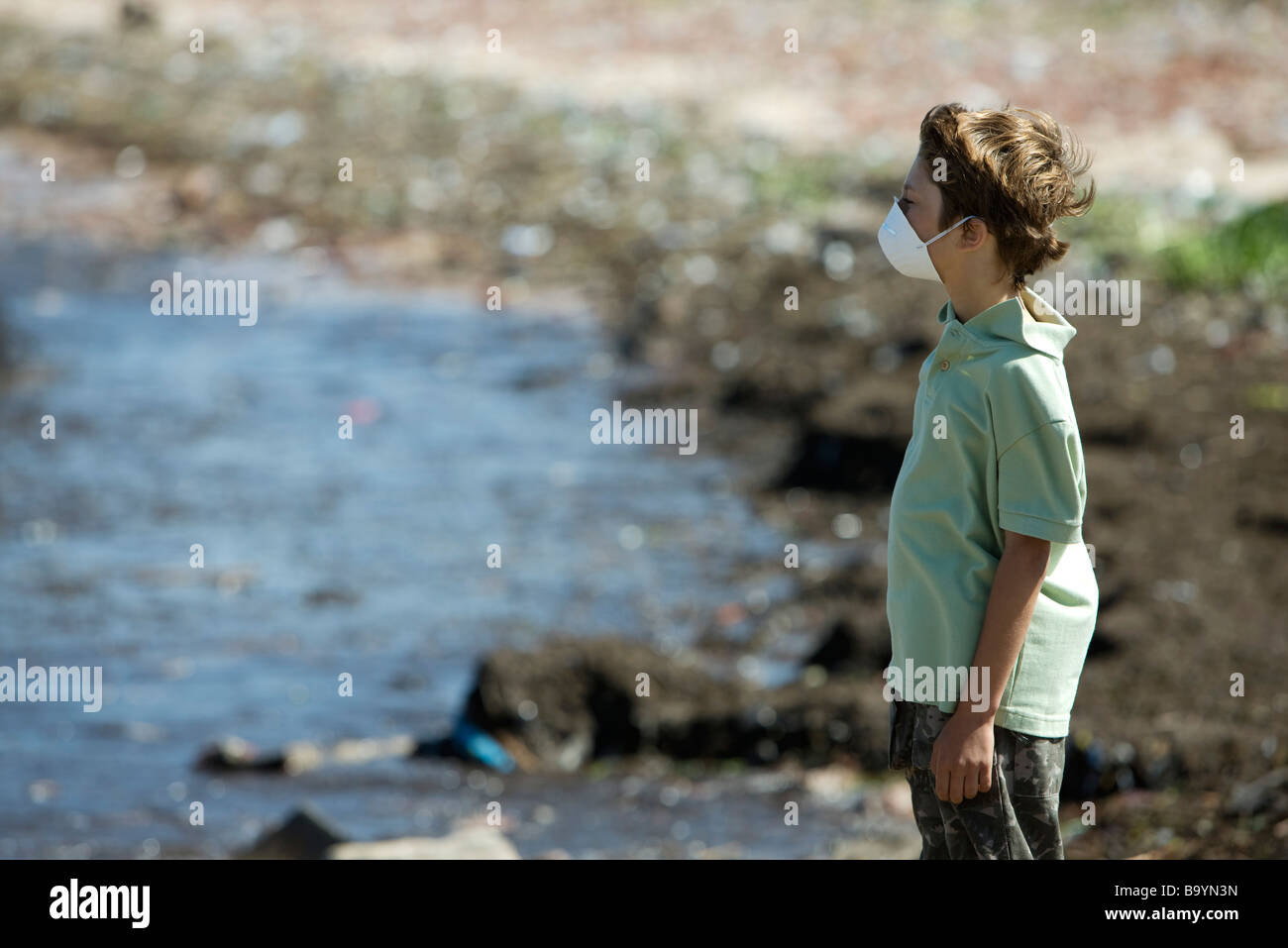 Boy wearing pollution mask, standing on polluted shore Stock Photo