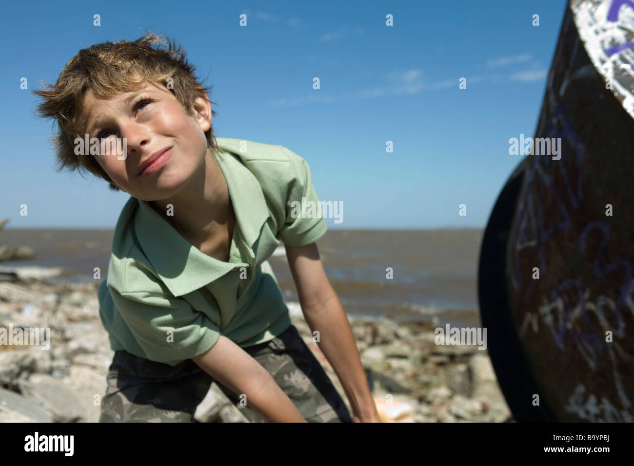 Boy on polluted shore, pulling large piece of scrap metal, close-up Stock Photo