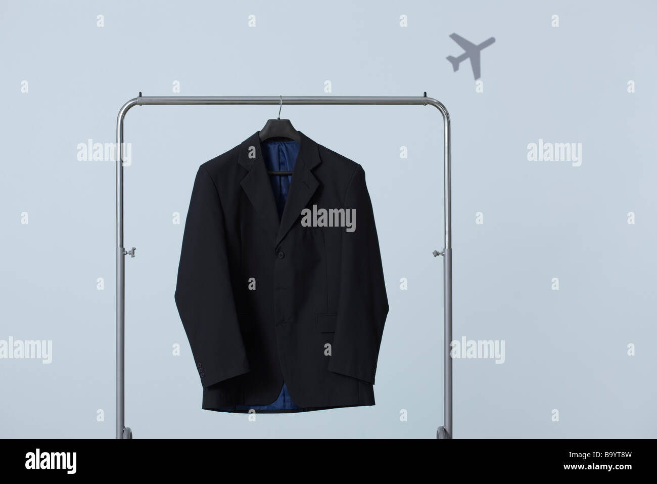 Man's suit jacket hanging on clothes rack, airplane in background Stock
