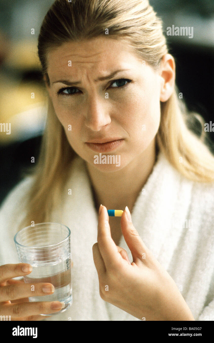 Woman holding pill and glass of water, frowning at camera Stock Photo