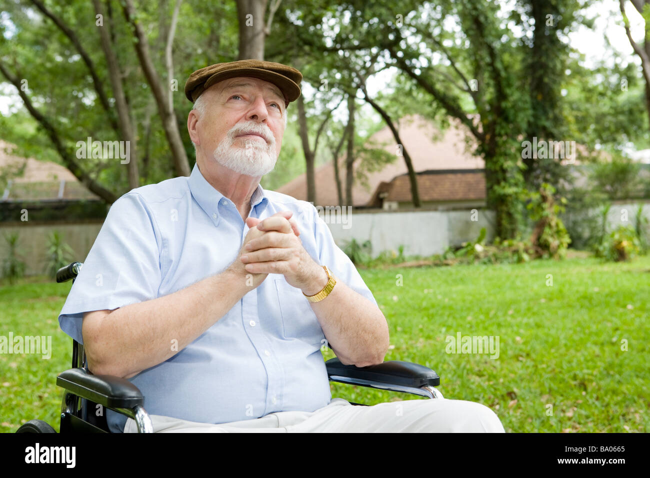 Senior man in wheelchair praying in a beautiful outdoor setting Stock Photo