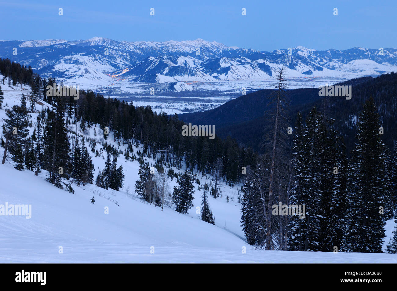 Teton Pass National Forest at dusk with lights of Jackson Wyoming and the Rocky Mountains Jackson and Pinnacle Peaks in winter Stock Photo