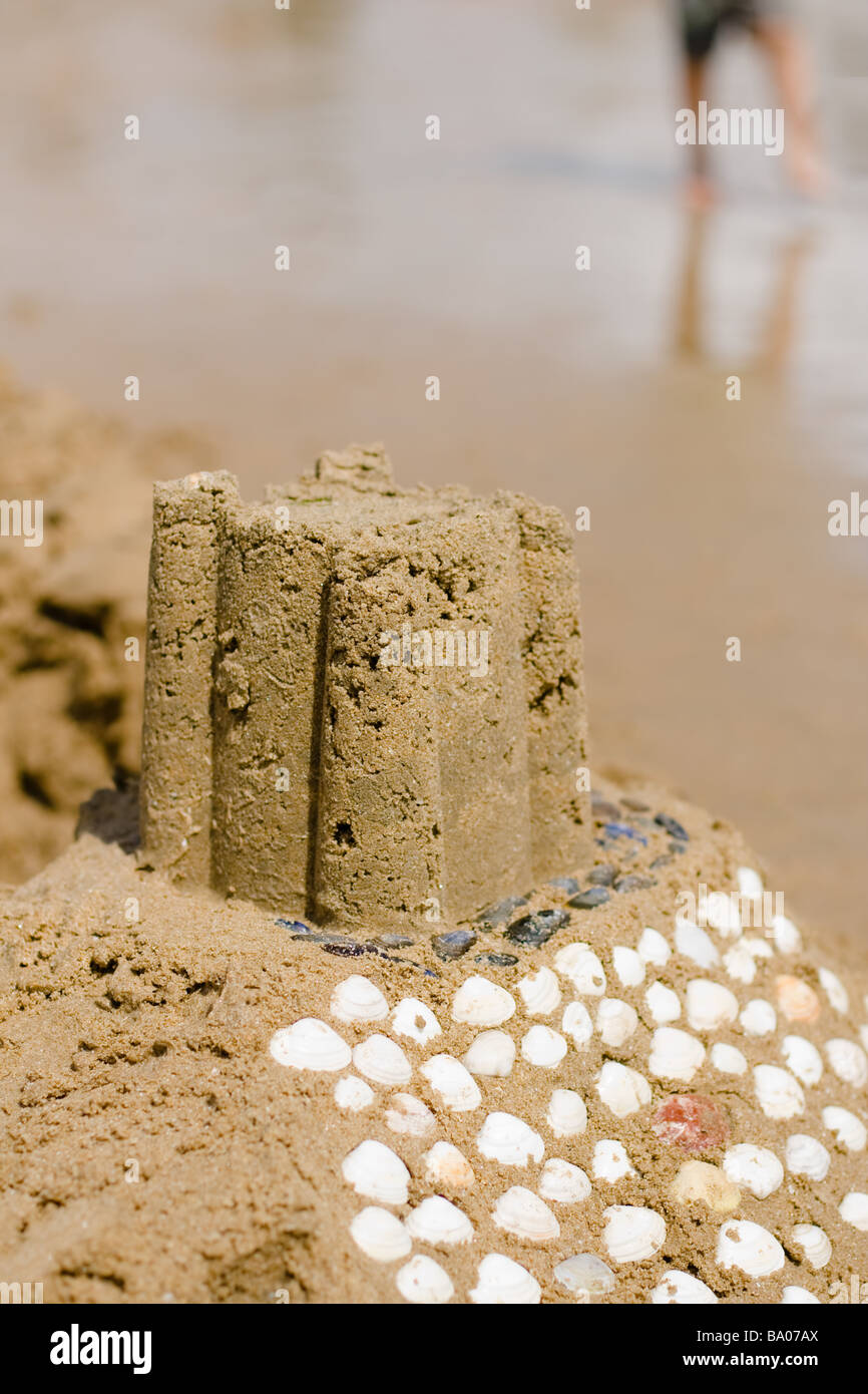 A sand castle decorated with seashells in the foreground with a boy&rsquo;s