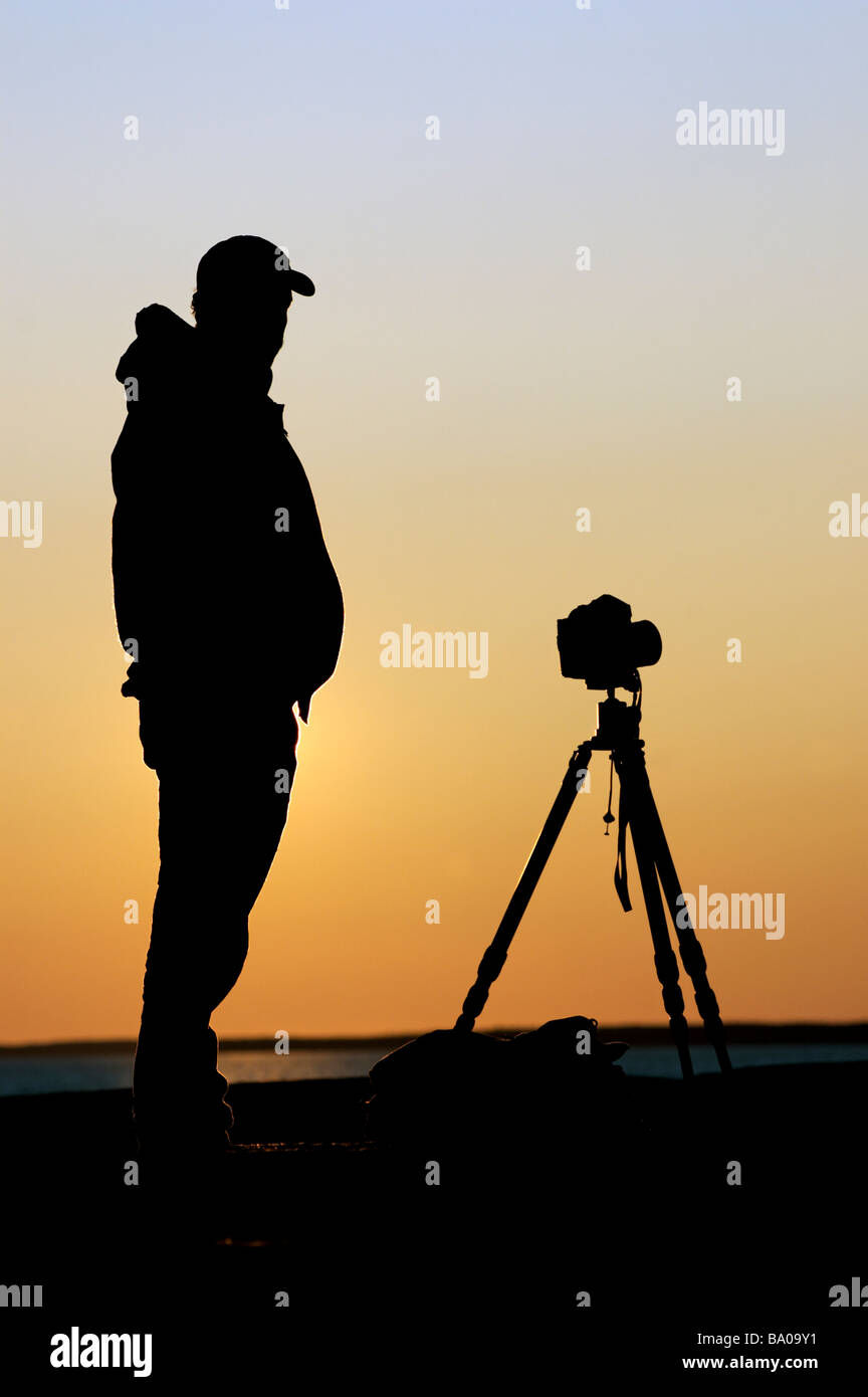 A photographer silhouetted against the setting sun Stock Photo