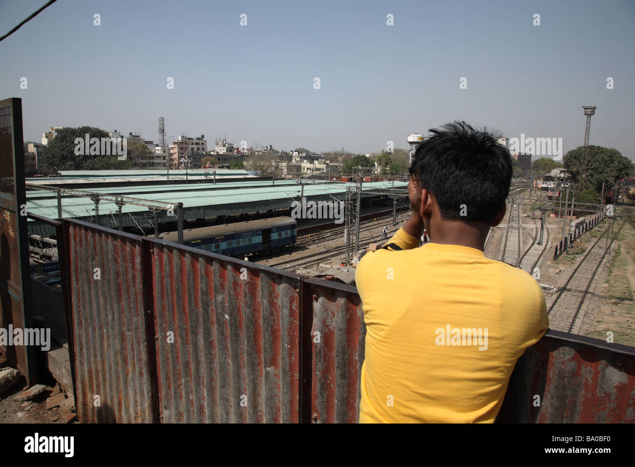 A boy watches trains arriving below at New Delhi train station, Delhi India Stock Photo