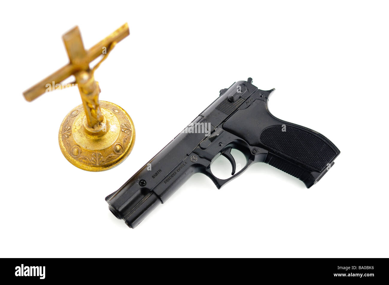 Handgun beside an old brass crucifix NOTE Handgun is imitation toy and marked accordingly Stock Photo
