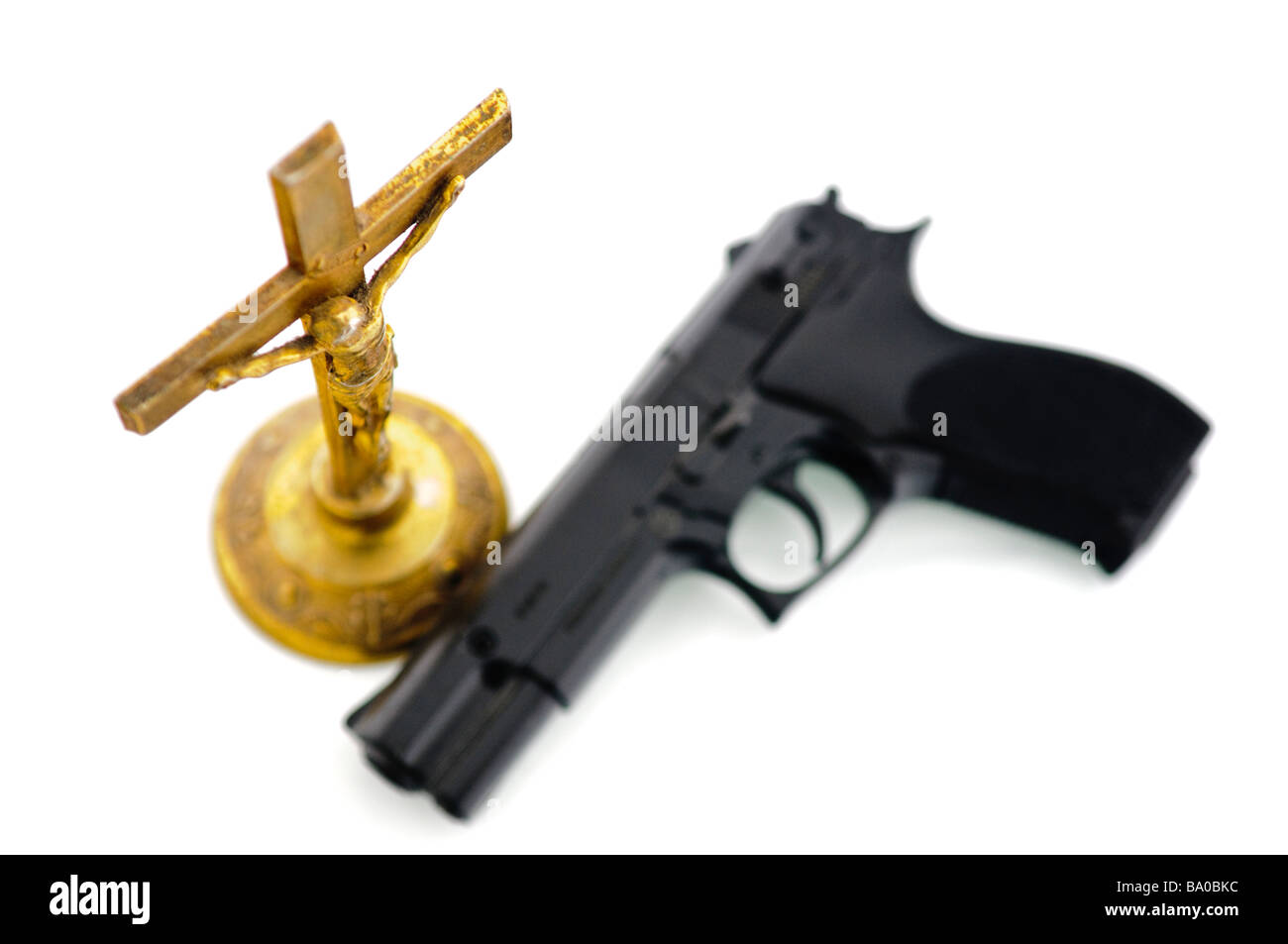 Handgun beside an old brass crucifix NOTE Handgun is imitation toy and marked accordingly Stock Photo