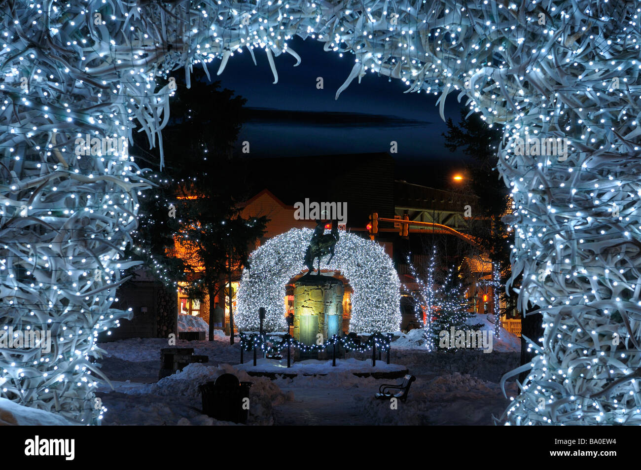 Bright Christmas lights on Elk antler arches in Jackson Wyoming USA town square in winter at twilight with cowboy on bucking broncho statue Stock Photo
