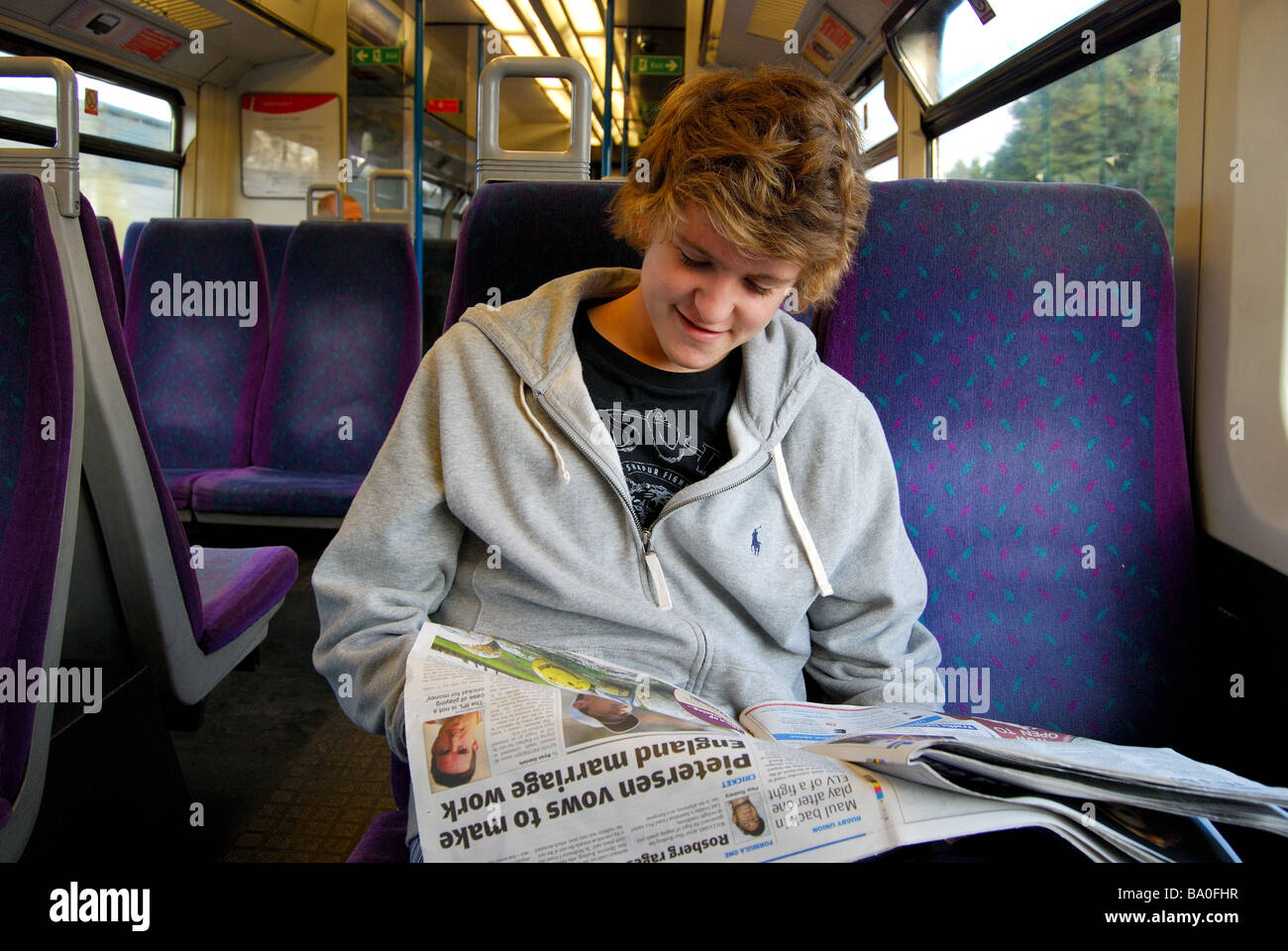 Teenage boy reading paper on train, Berkshire, England, United Kingdom Stock Photo