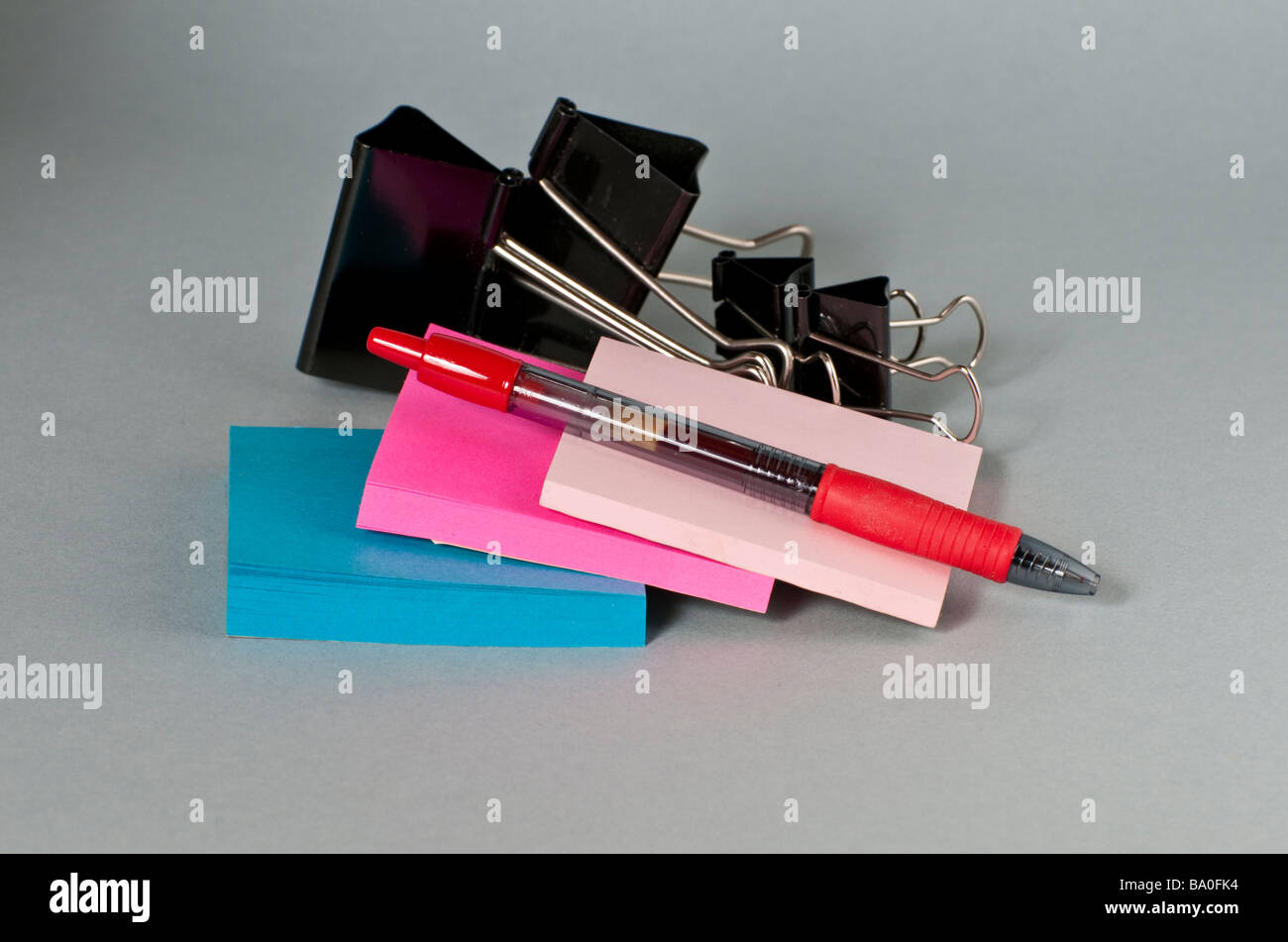 Three colorful sticky postit note pads with steel bulldog paper clips and a pen Stock Photo