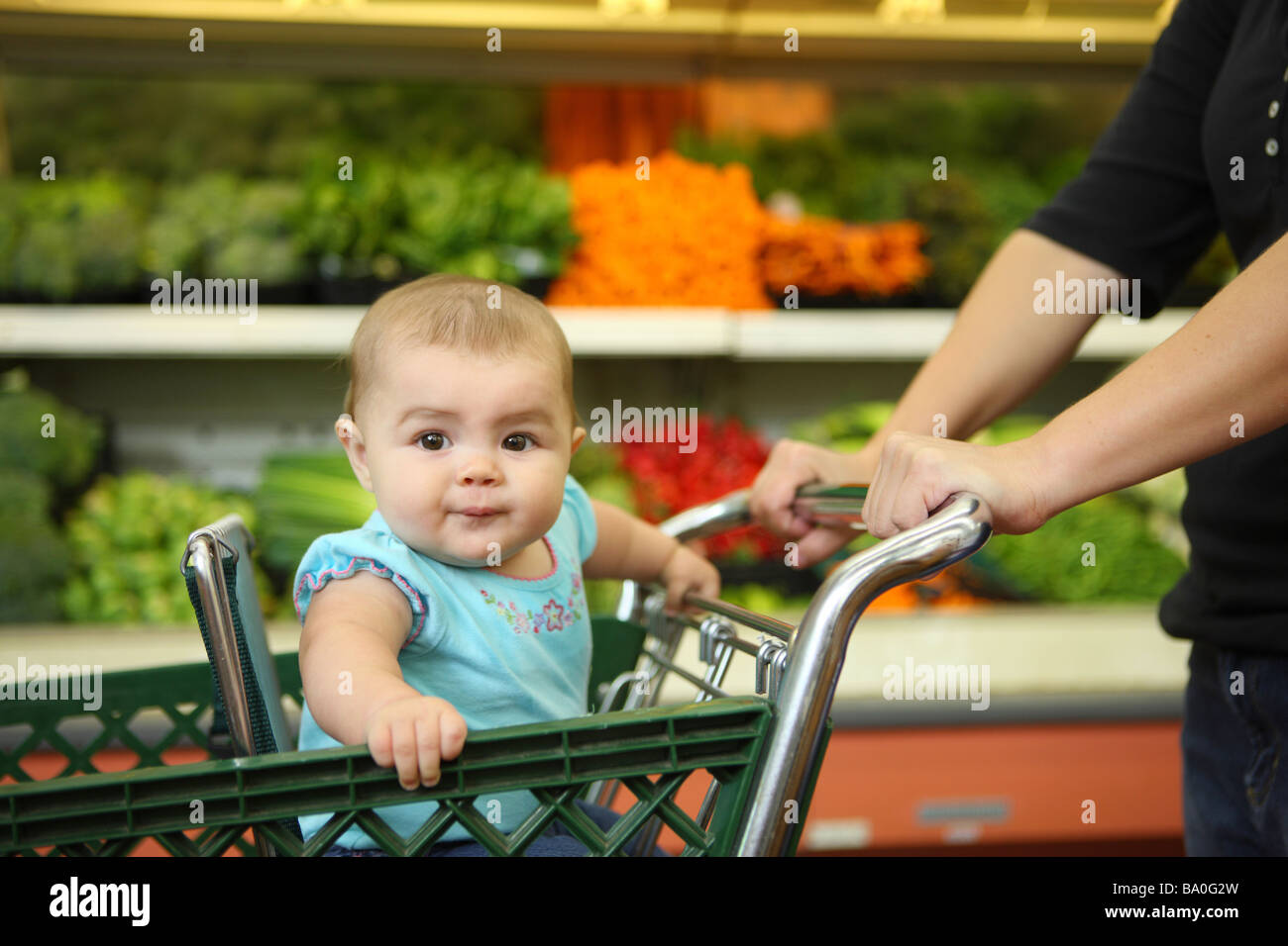Baby in shopping cart in produce section of grocery store Stock Photo