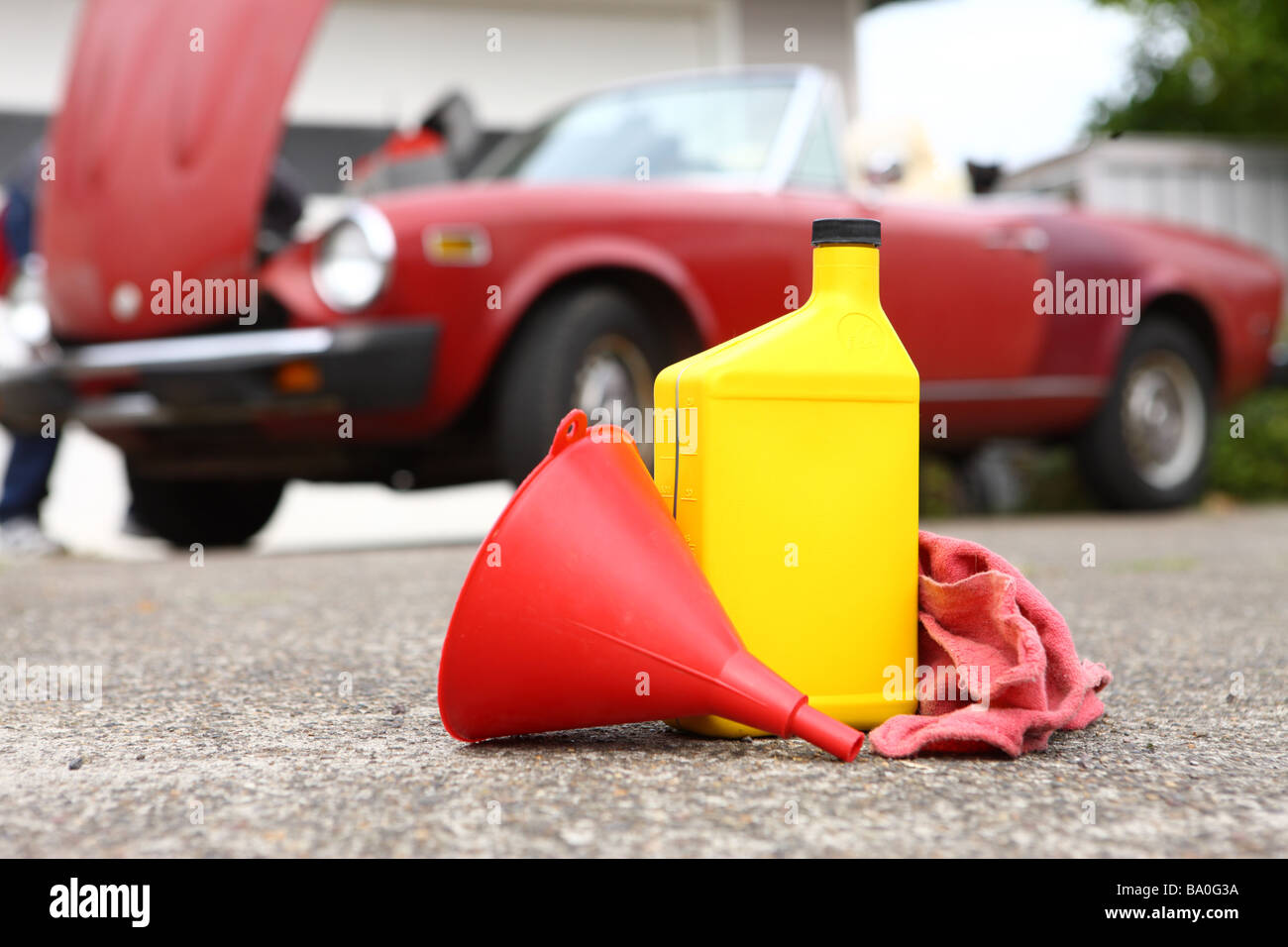 Oil bottle funnel and rag with classic car in background Stock Photo