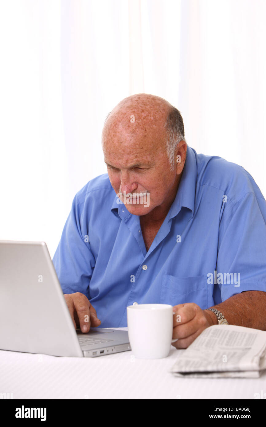 Senior man working on laptop with coffee and newspaper Stock Photo